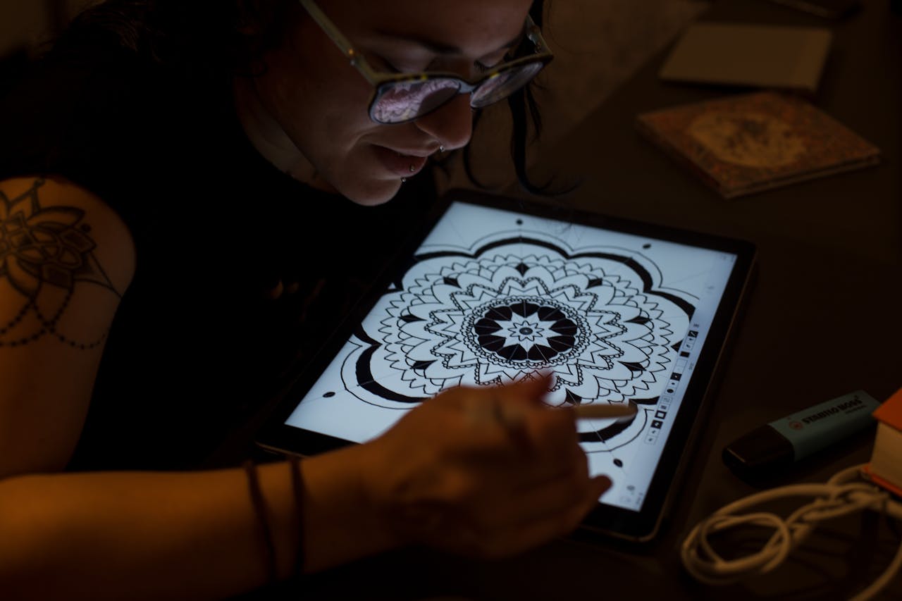 about-01 A digital artist uses a tablet for creative mandala design work in a dimly lit setting.