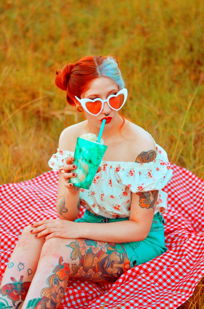 Stylish woman with tattoos enjoying a drink at a summer picnic.