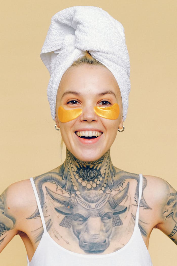 about-03 Smiling tattooed woman with eye patches and towel wrapped hair, portrait in studio.